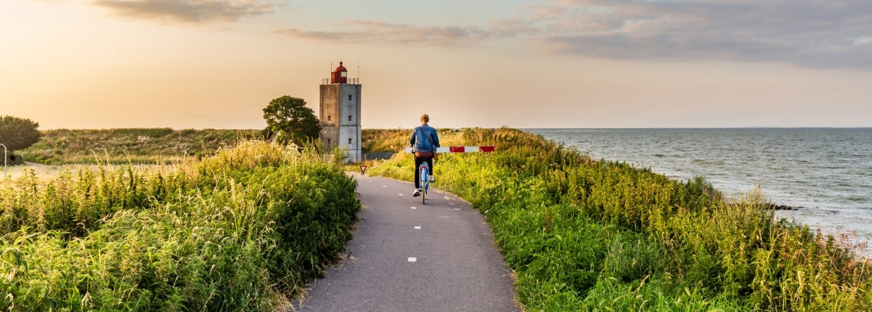 Meisje fietsen naar vuurtoren De Ven bij Edam tijdens zonsondergang in Noord-Holland in Nederland