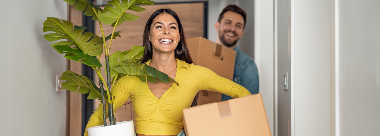 Jong stel is aan het verhuizen en hebben dozen en een plant in hun handen